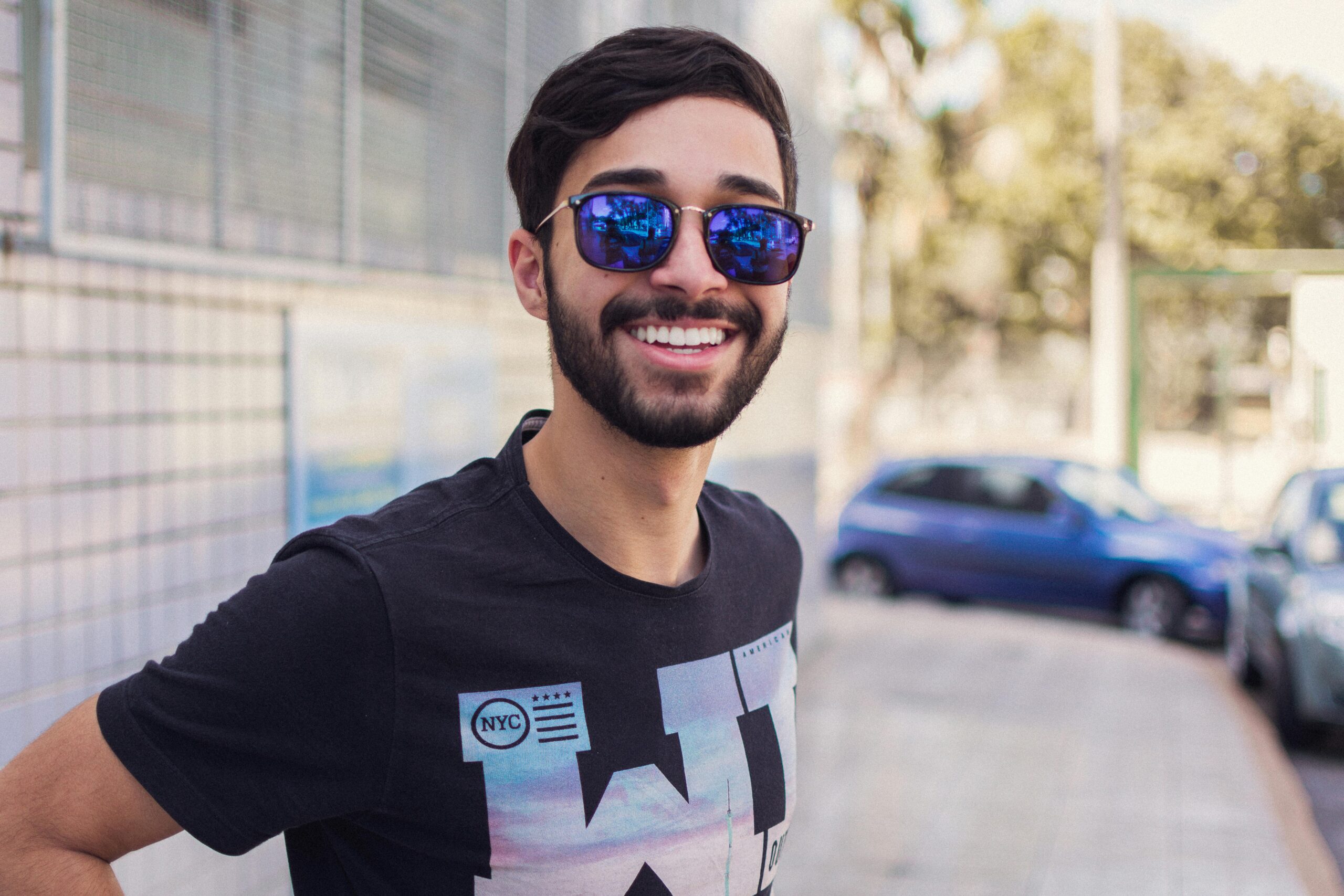 Portrait of a smiling man wearing sunglasses outdoors, showcasing modern fashion and style.